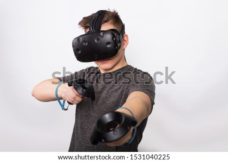 A young man holds controllers for a viar game. A teenager plays with virtual reality glasses and considers joysticks and gamepads.