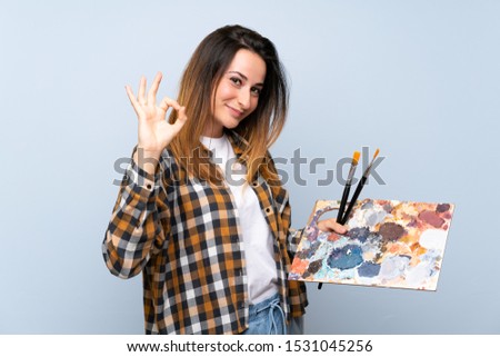Young painter woman over isolated blue background showing ok sign with fingers