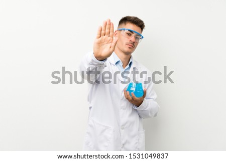 Young scientific holding laboratory flask over isolated background making stop gesture with her hand