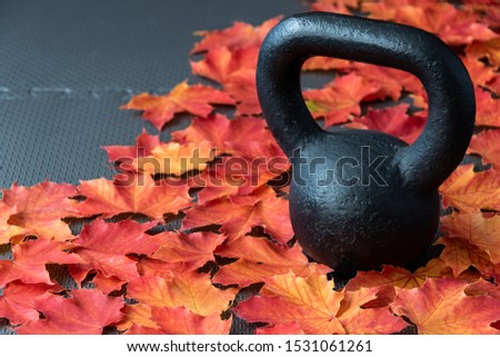 Black iron kettlebell on a black rubber gym floor, with orange and yellow maple leaves, fall fitness
 Royalty-Free Stock Photo #1531061261