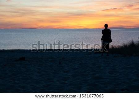 Person watching an taking a picture of sunset at the beach in Cape Cod