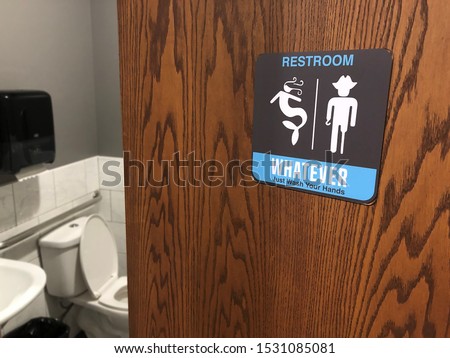 Partially open restroom door and sign with gender inclusive language and symbols stating WHATEVER JUST WASH YOUR HANDS. Toilet, sink, grab bar and towel dispenser are seen inside.