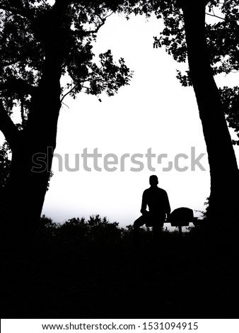 Silhouette of young man sitting on edge of mountain and looking to the sky. Dreaming and thinking alone person at forest. Solitude and loneliness concept. Royalty-Free Stock Photo #1531094915