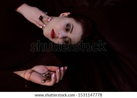 vampire girl with black hair and white skin lies and holds a cross for Halloween