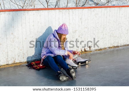 Lovely young woman sitting on ice ring and tieing shoelaces. Girl is going to skating on ice in a winter frosty day. Copy space