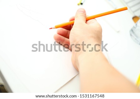 Male hand holding orange pencil ready to draw closeup