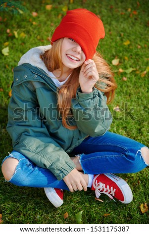 Joyful child girl sits on a grass under autumn leaf fall. Happy autumn mood.
