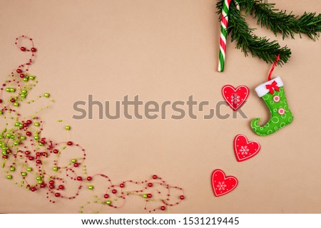 Festive Christmas beads, a red-green boot for candies hanging on a Christmas tree branch, with a lollipop lying in the form of a cane, with a red heart, on a beige background.Copy space.Decorations.