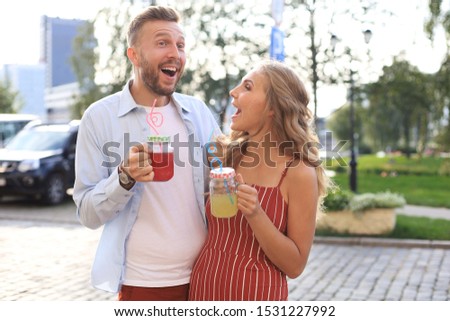 Beautiful young couple walking through the city street, smiling and drinking fresh cocktails
