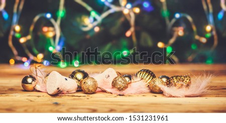 Cute Christmas toys with light pink feathers on wooden table against Christmas tree on background