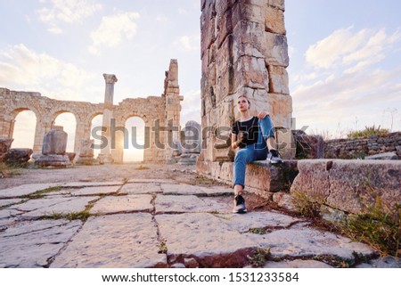 Tourism and hobby. Happy young woman taking photo of ancient antique city Volubilis. Traveling by Morocco.