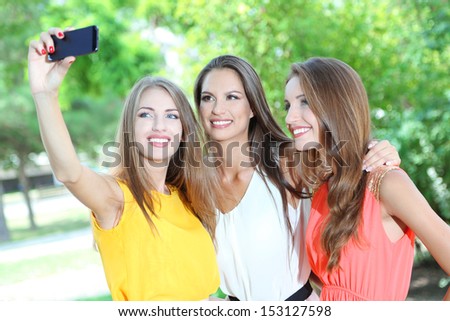 Three beautiful young woman  taking picture in summer park