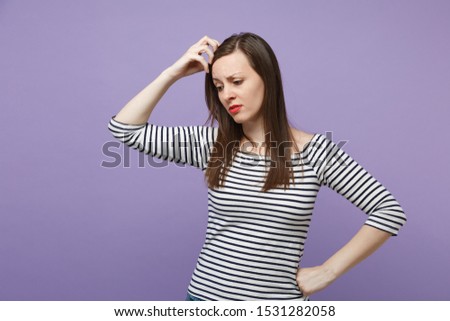 Preoccupied young brunette woman in casual striped clothes posing isolated on violet purple background studio portrait. People lifestyle concept. Mock up copy space. Looking down putting hand on head