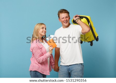 Young joyful couple two friends guy girl in white pink t-shirts posing isolated on pastel blue background. People lifestyle concept. Mock up copy space. Hold passport boarding pass, ticket, suitcase