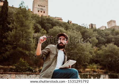
Young man sitting in the street of Granada, Spain, drawing in his travel notebook. Enjoying the sunset, developing his creativity. Relaxed and carefree. Lifestyle.