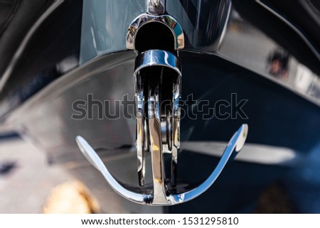 Stylised shot of a bow anchor, made of highly polished stainless steel protruding from the bow of a sports boat. The anchor is the only aspect in focus, the rest is blurred for effect.