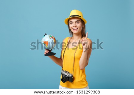 Traveler tourist woman in yellow summer casual clothes, hat with globe, camera isolated on blue background. Female passenger traveling abroad to travel on weekends getaway. Air flight journey concept