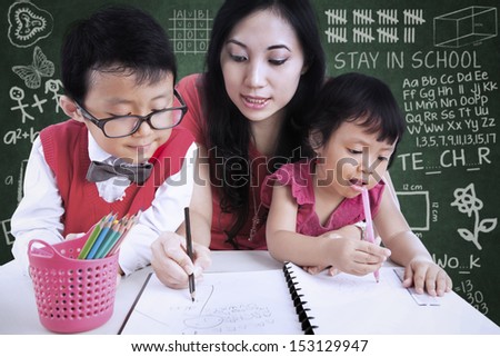 Beautiful female teacher help children write letters in class
