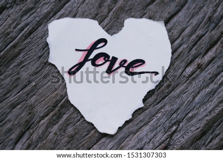 Piece of paper with text "Love" on wooden table closeup blur background