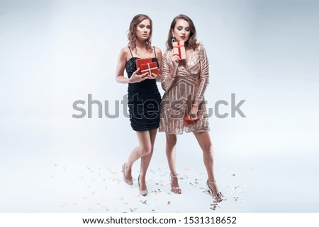 Two young women with red presents in hands isolated on white background. Christmas and New Year celebration. Copy space.
