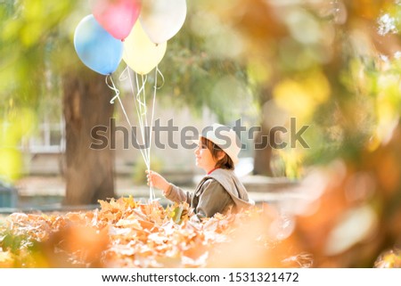 Kid having fun in autumn leaves with balloons