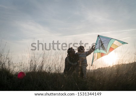 Father and son with kite on sunset meadow silhouette