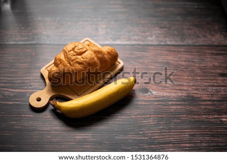 Fresh croissants with banana on wooden background dark tone.