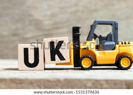 Toy forklift hold letter block k to complete word UK (abbreviation of united kingdom) on wood background