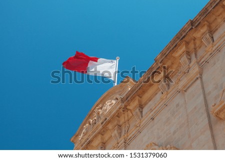 Maltese flag mounted on an old stone building waving over blue sky. Valetta, Malta
