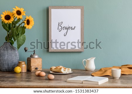 Stylish and sunny interior of kitchen space with wooden table, brown mock up photo frame, breakfast and sunflowers. Scandinavian home decor with kitchen accessories. Template. Eucalyptus color concept