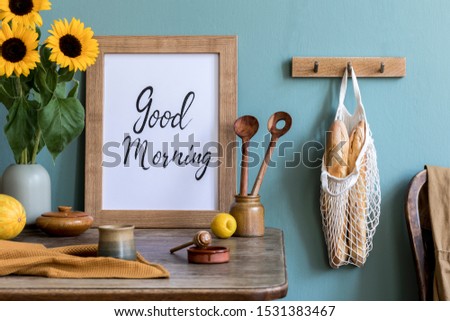 Stylish interior design of kitchen space with wooden table, mock up frame, bag with bagles, honey, sunflowers in vase, vegetables and kitchen accessories. Vintage concept of kitchen space..
