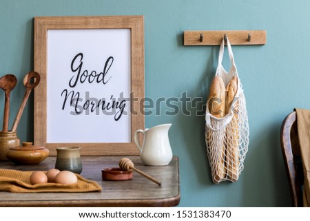  Stylish interior design of kitchen space with mock up photo frame, wooden table,  cup of tea, eggs, bagles and kitchen accessories. Cozy home decor of kitchen space. Template. 