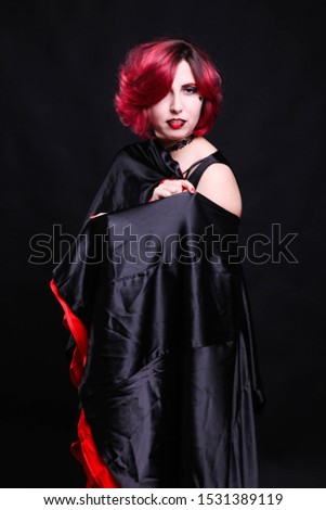 Girl with red hair dressed in a mantle on a black background. Halloween concept.