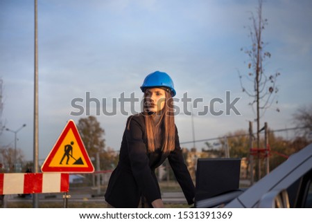 A beautiful young woman civil engineer is on a construction site and she is holding a computer with a project in her hands while it is sunset.