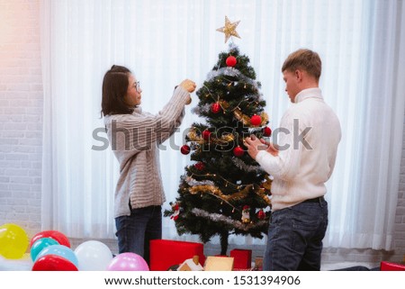 Happy man and woman in winter dress decorate the Christmas tree in the home room. Christmas holidays.