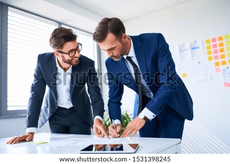 Two businessmen standing over documents in office signing contract and talking