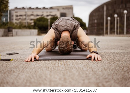 Young athletic guy doing workout. Fitness outdoors. Stretching. Urban background.