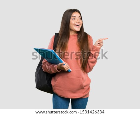 Young student woman holding notebooks pointing finger to the side over isolated grey background