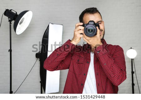 Young photographer with camera and professional studio equipment on grey background