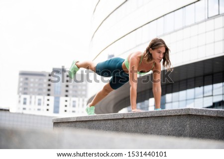 Fit young woman doing plank exercise outdoor in urban environment
