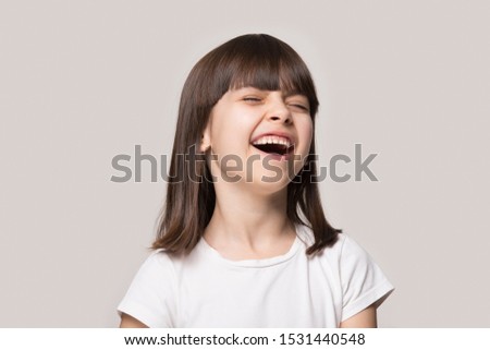 Headshot of excited small preschooler girl isolated on grey studio background laugh at funny joke, overjoyed happy little child have fun giggle chuckle feel amused, kid humor, entertainment concept
