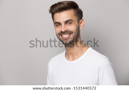 Close up headshot portrait of smiling caucasian young man in white t-shirt isolated on grey studio background look at camera, happy millennial bearded male posing show healthy teeth