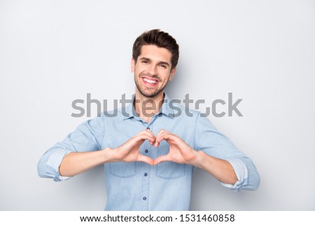Portrait of positive cheerful man feel content on 14-february make heart with his fingers show feelings of love romance wear denim jeans style  outfit isolated over grey color background