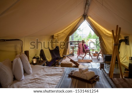 glamping trip - woman sitting outside luxury camping tent enjoying view of forest Royalty-Free Stock Photo #1531461254