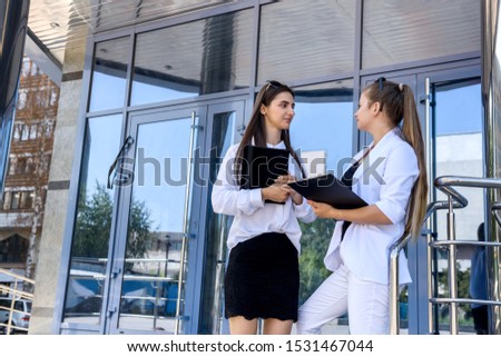 Two businesswoman holding tablets and talking opposite office building