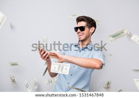 Photo of cheerful excited ecstatic overjoyed man throwing money away showing his wealthiness wearing denim isolated over grey color background