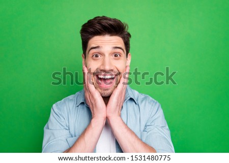 Close up photo of amazing macho guy holding arms on cheeks looking on unbelievable low prices wear casual denim shirt isolated over green color background