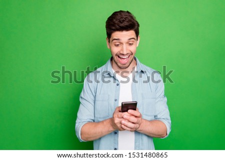 Photo of amazing guy holding telephone read new cool instagram post comments overjoyed positive reviews wear denim shirt isolated green color background