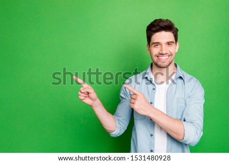 Photo of amazing salesman guy in excited mood indicating finger to empty space advising cool shopping prices wear casual denim shirt isolated green color background