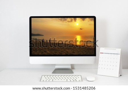 working space and the picture of sunset on the Phuket beach on the mockup desktop computer, calendar and accessories on white desk. holiday concept. clipping path.